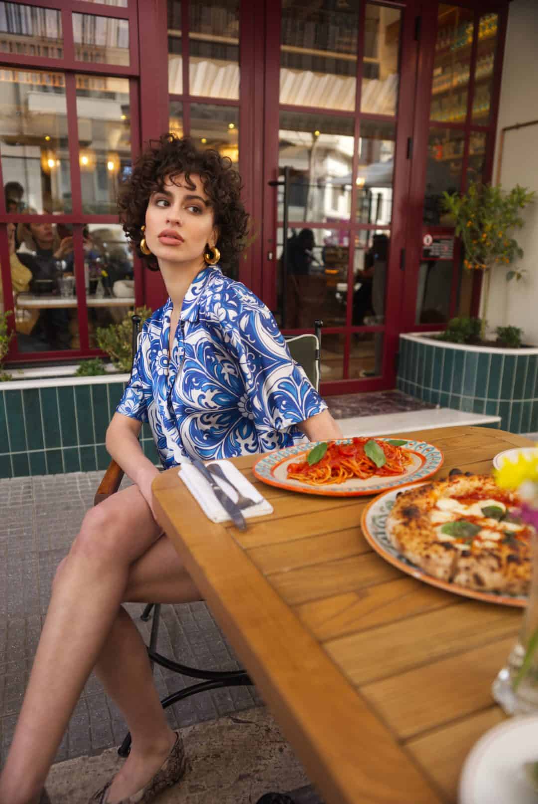 Woman sitting at a table with pizza and pasta in an outdoor restaurant setting