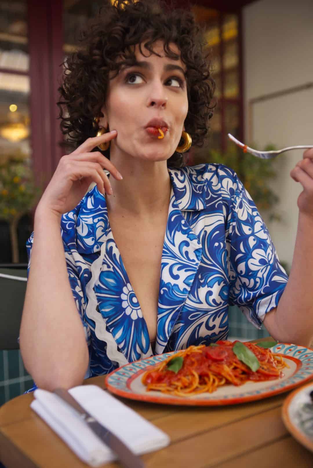 Woman in a blue and white patterned dress eating spaghetti at a restaurant.