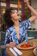 Woman in a blue and white patterned outfit eating spaghetti at an outdoor restaurant.