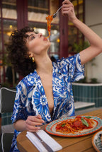Woman in a blue and white patterned outfit eating spaghetti in an outdoor setting.