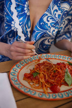 Person in a blue and white patterned outfit eating spaghetti with a decorative plate.