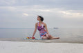 Woman sitting on a beach with a colorful dress and towel.