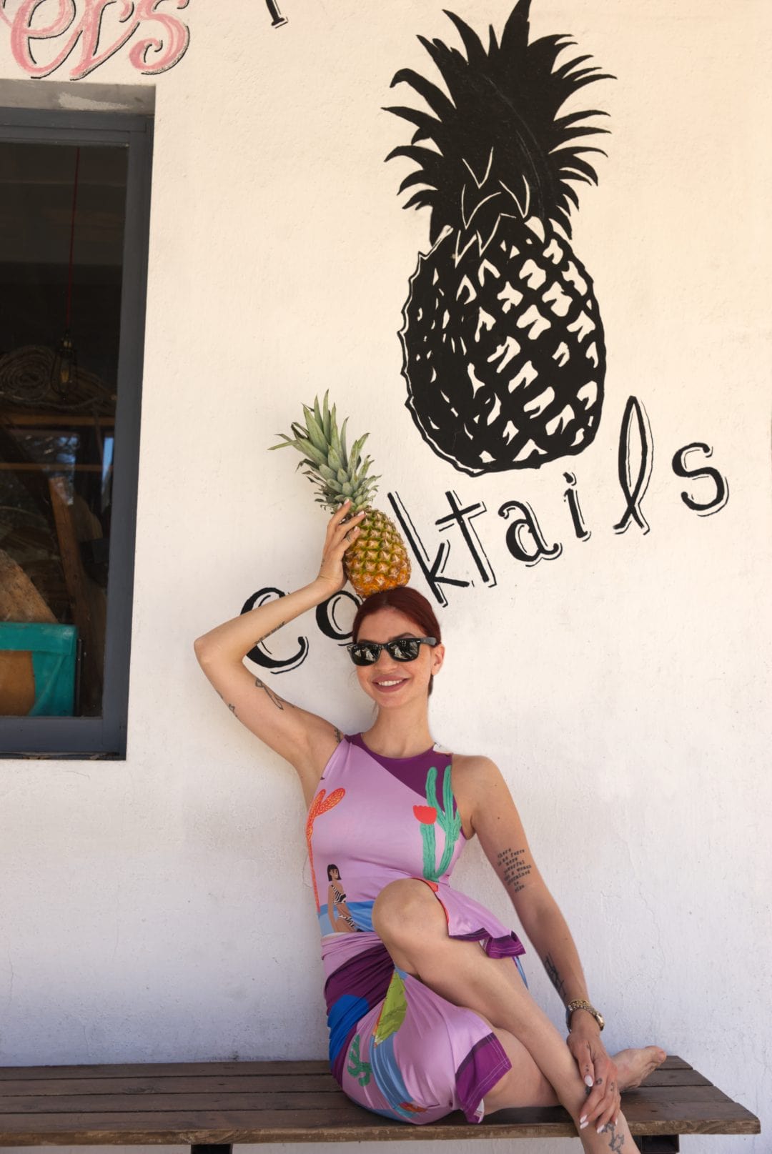 Woman holding a pineapple with 'Cocktails' written on the wall
