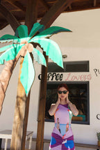 Woman in a colorful dress standing next to a palm tree in front of a coffee shop.
