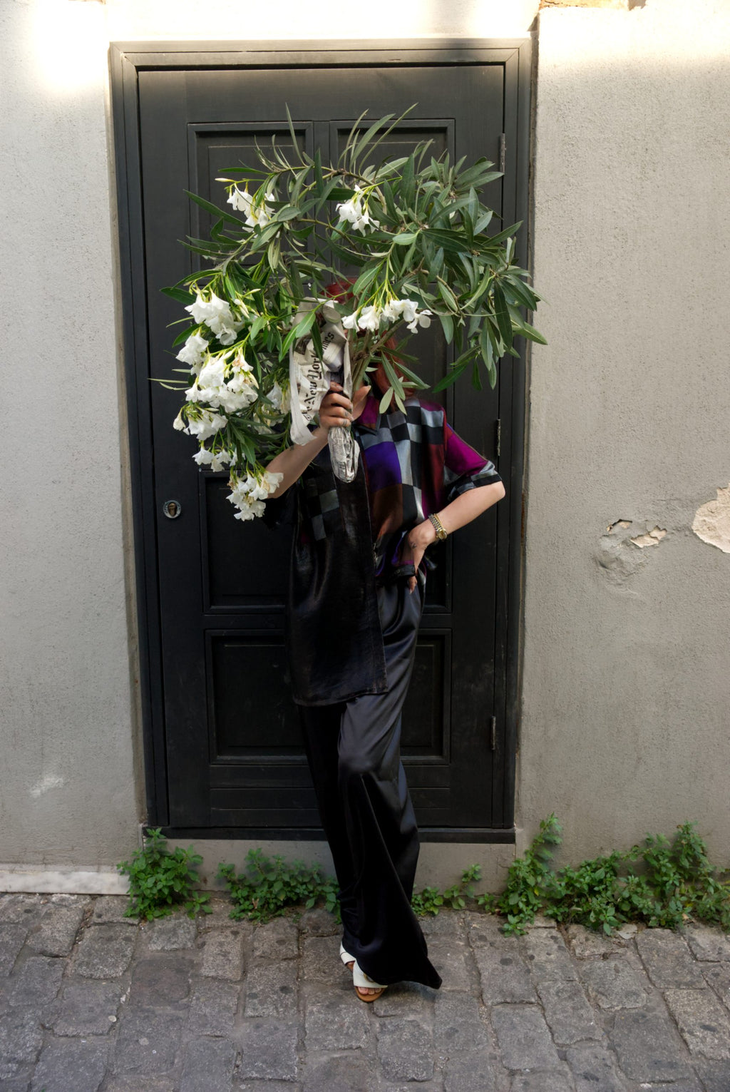 Person holding a bouquet of flowers against a black door on a street.