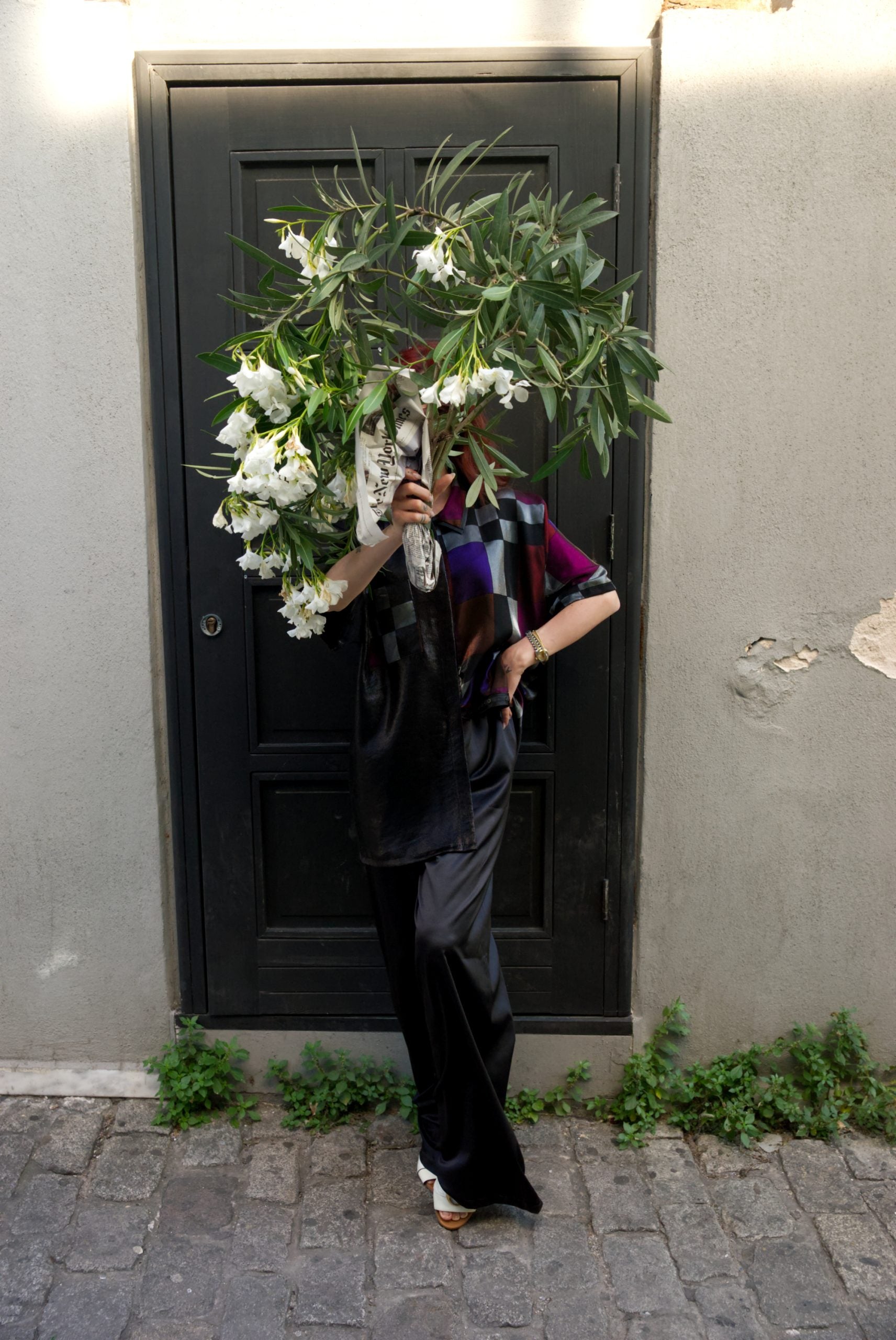Person holding a bouquet of flowers against a black door on a street.