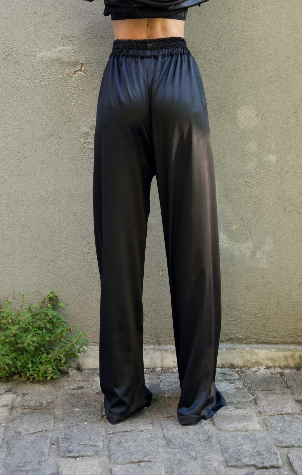 Person wearing black satin pants standing against a beige wall.