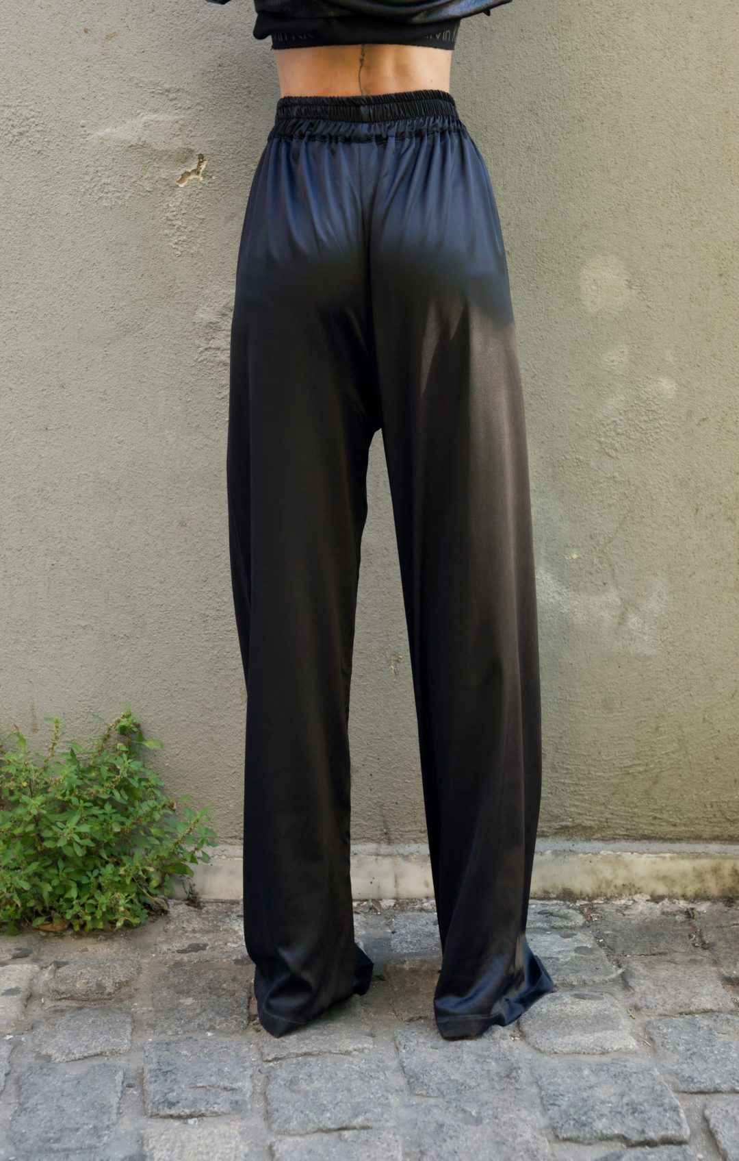 Person wearing black satin pants standing against a beige wall.