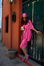 Woman in a pink outfit standing in front of a green door with a red wall.