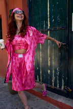 Woman in a bright pink outfit with a pattern, standing in front of a green door.