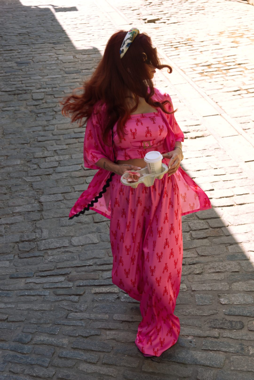 Woman in a pink dress with heart patterns walking on a cobblestone street.