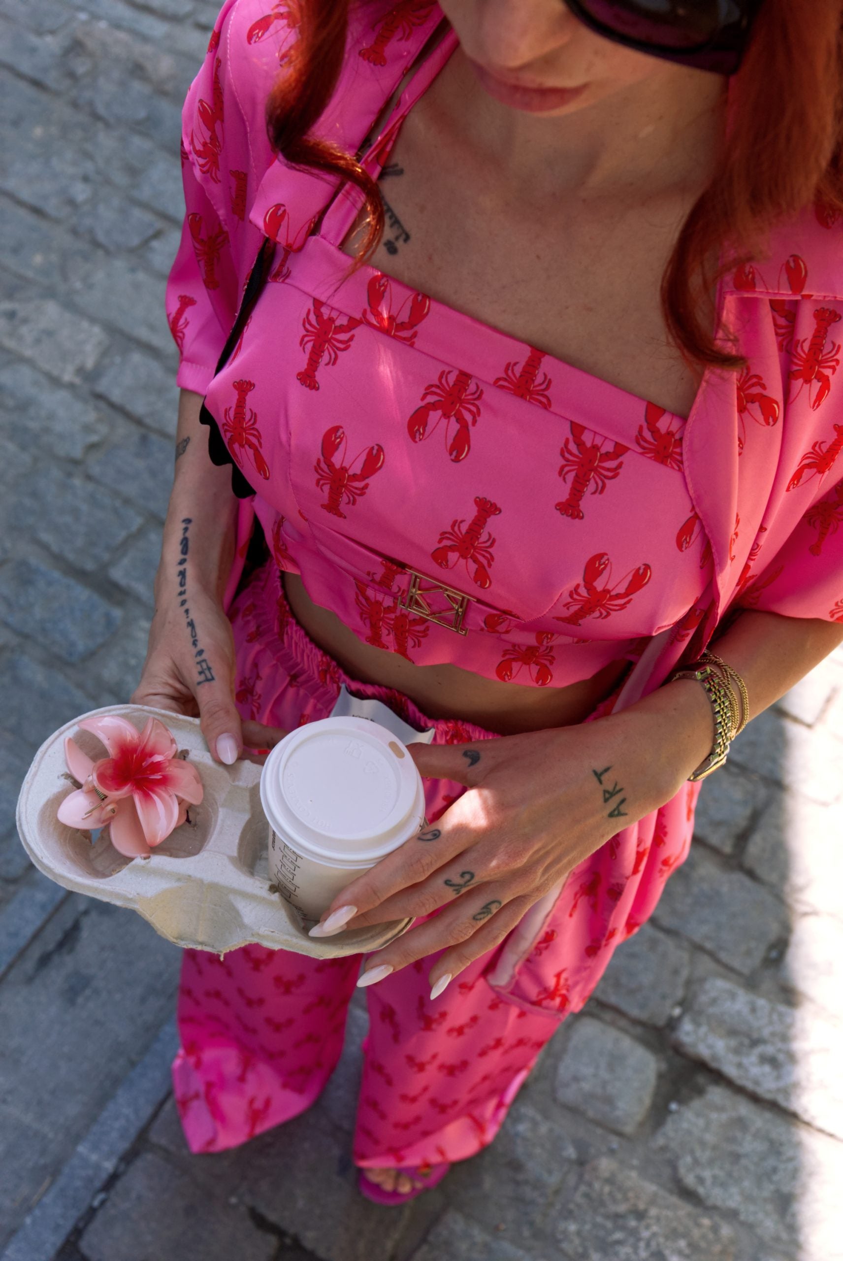 Person wearing bright pink pajama set holding a coffee cup and makeup palette.