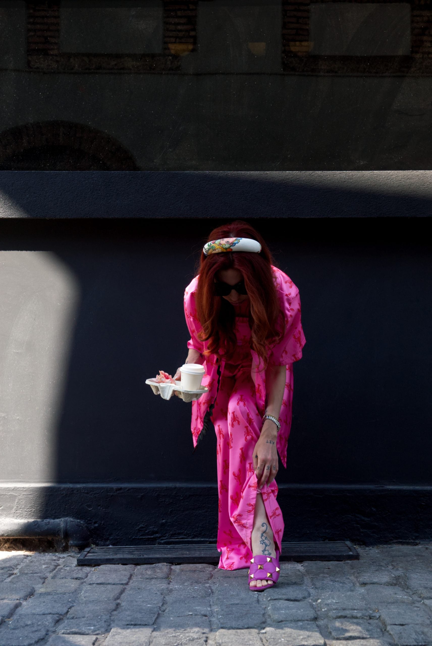 Person in a bright pink outfit standing against a dark wall.