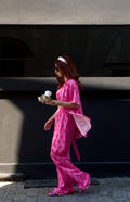Woman in a pink dress walking on a street with a black wall in the background