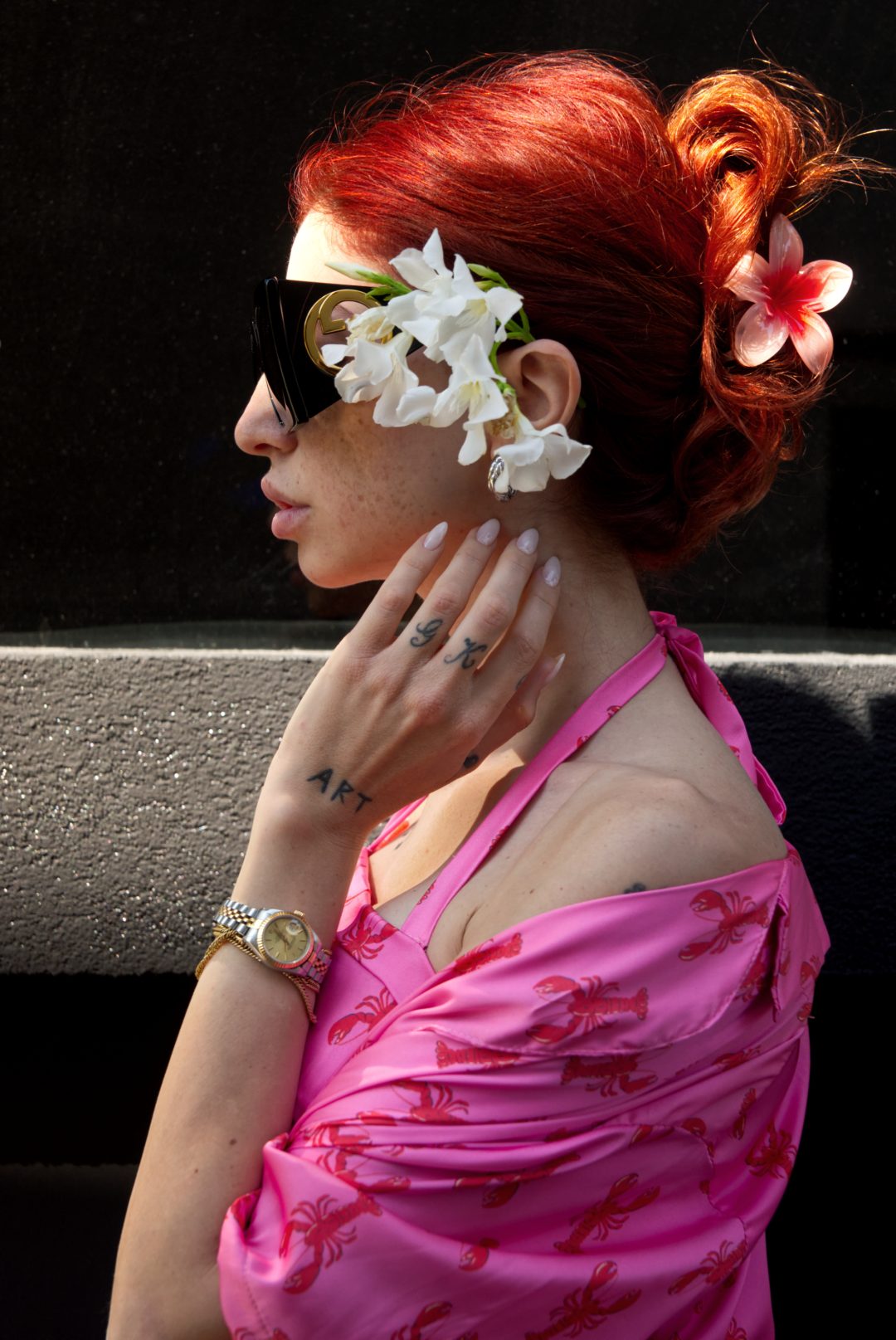 Person with red hair and floral headband wearing sunglasses and a pink top.