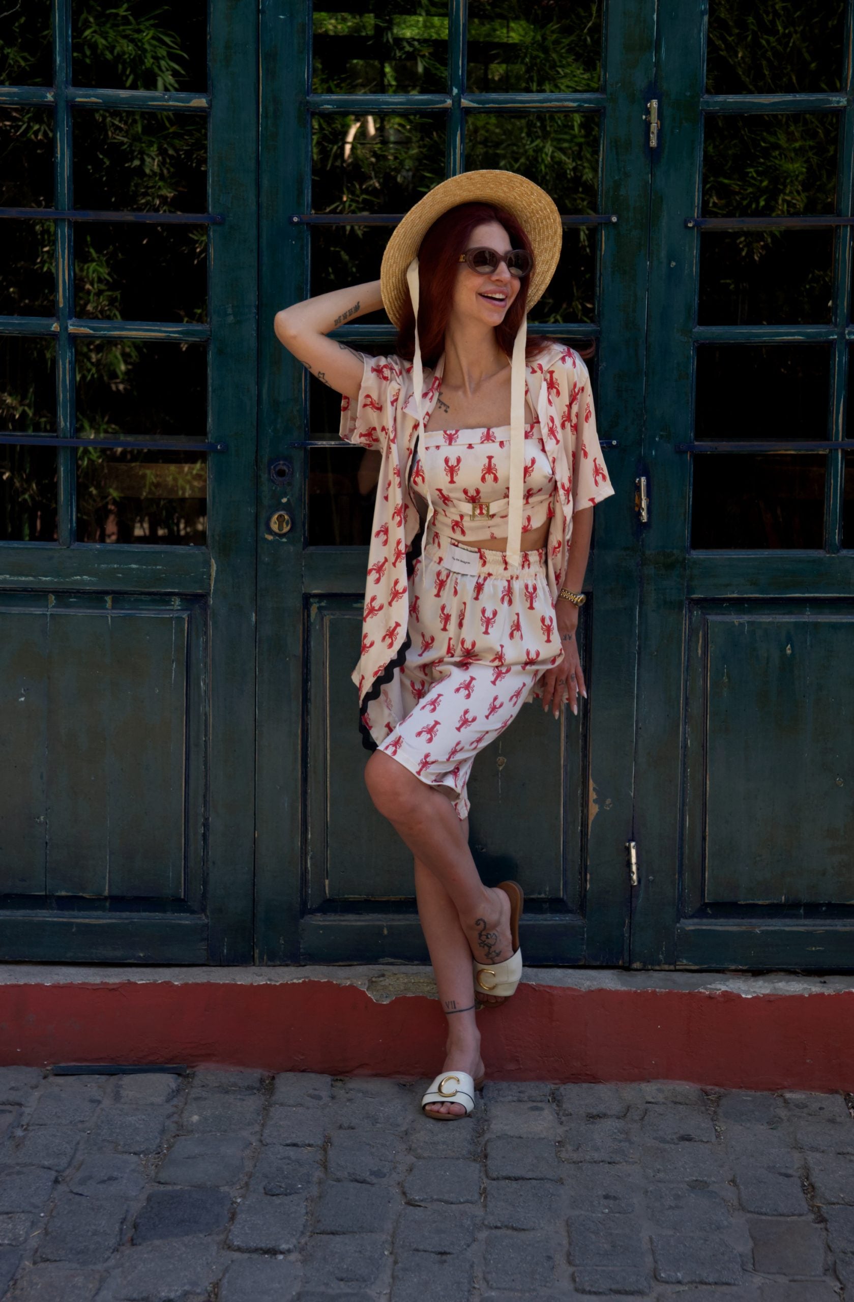 Woman in a floral dress and hat standing in front of a dark green door.