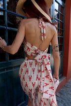 Woman wearing a dress with red patterns and a straw hat, standing in front of a building.