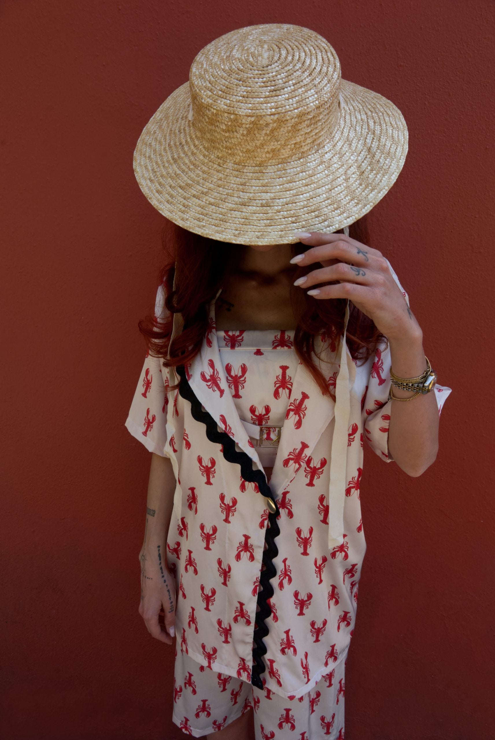 Person wearing a straw hat and a patterned outfit against a red background