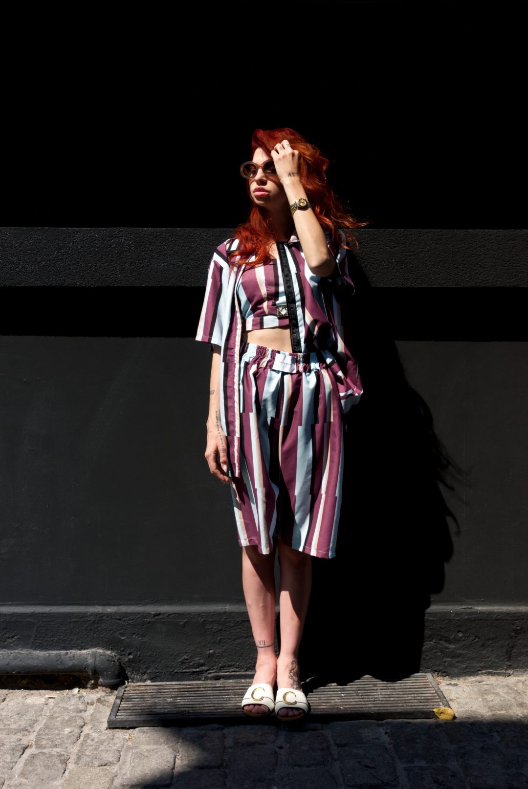 Woman in a striped outfit standing against a black and gray wall.