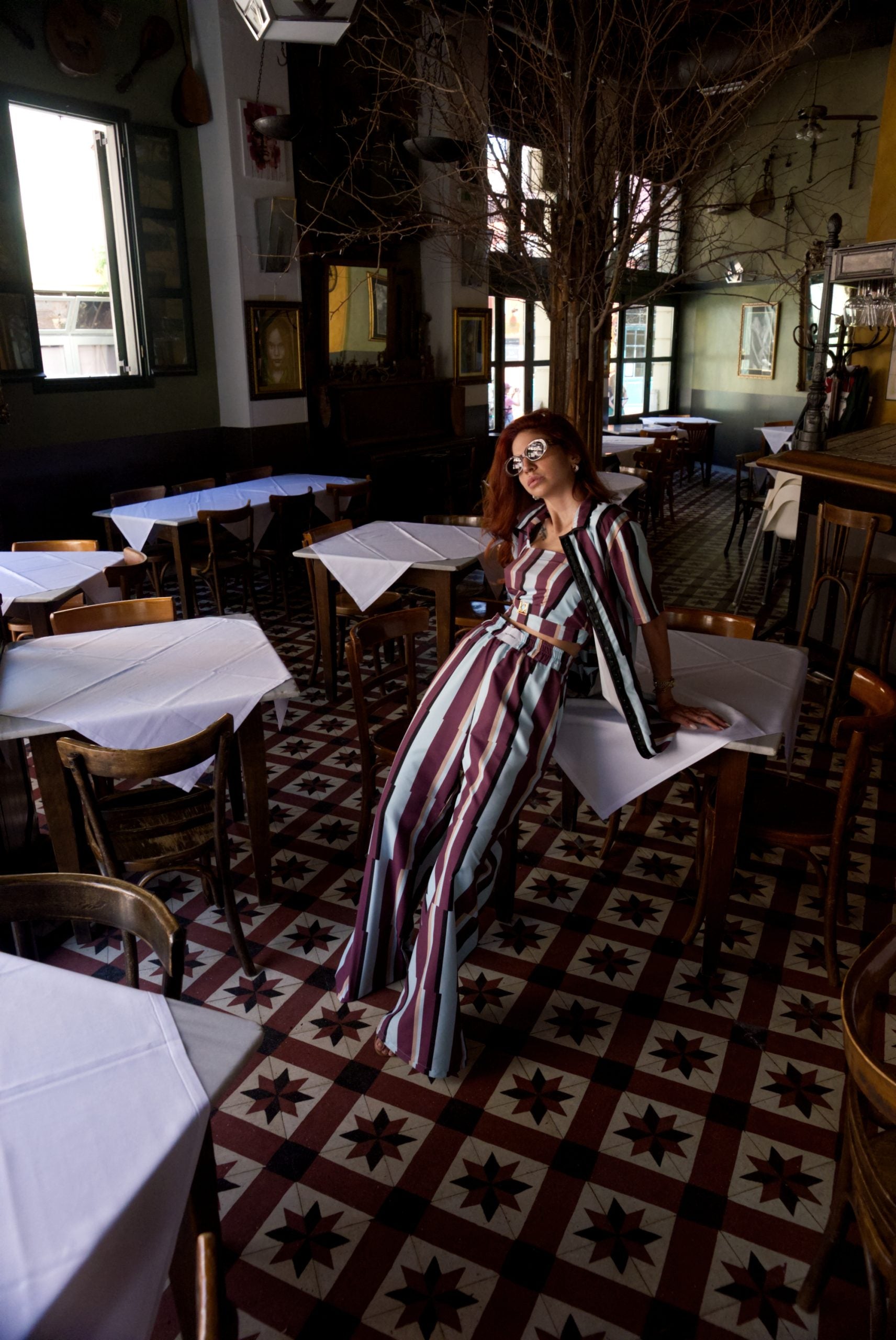 Woman in a striped dress sitting at a table in a restaurant with patterned floor and decor.