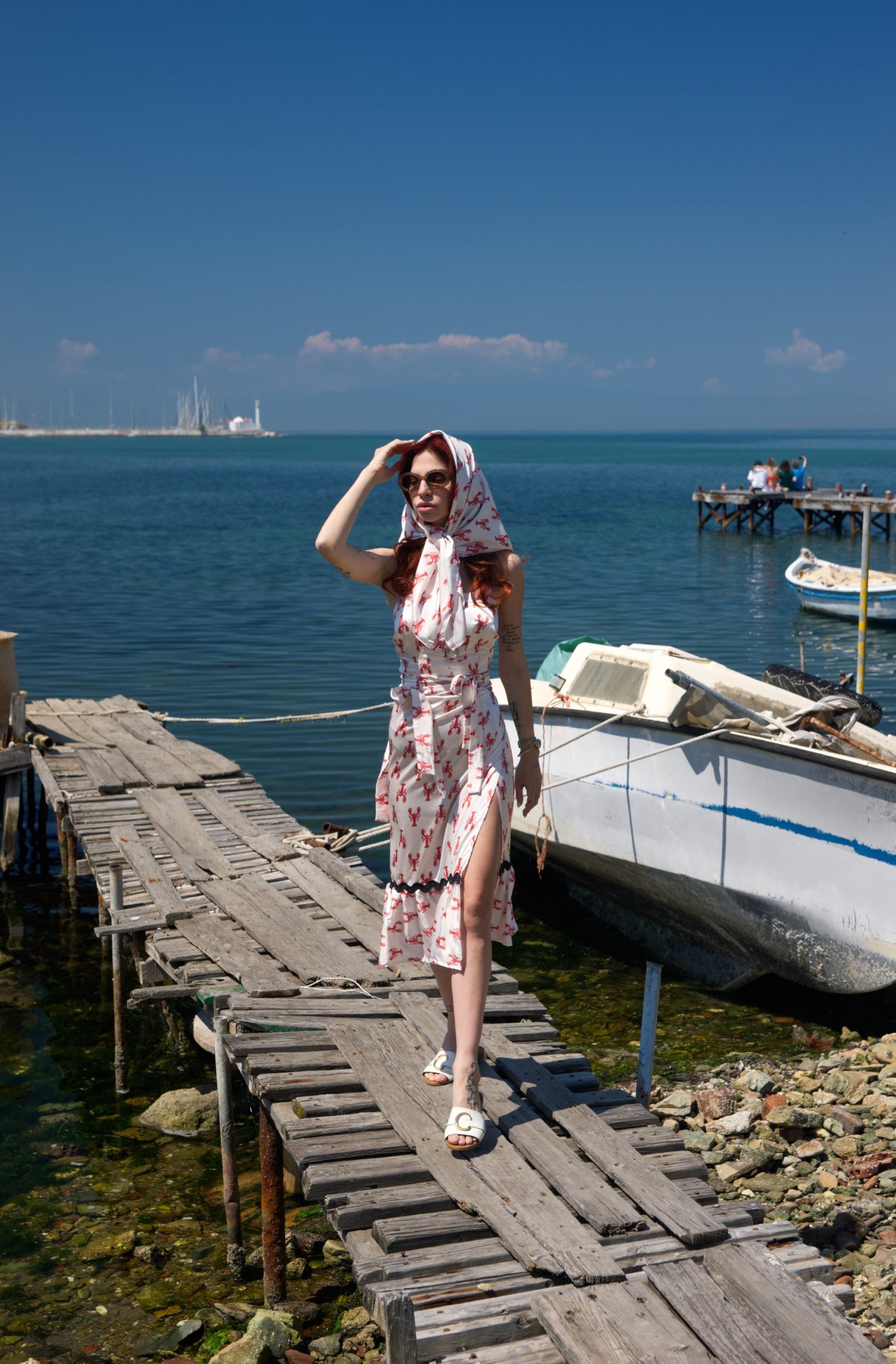 Woman in a floral dress standing on a wooden dock by the sea