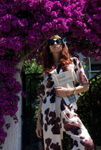 Woman in a patterned dress holding a book under a purple flowering tree