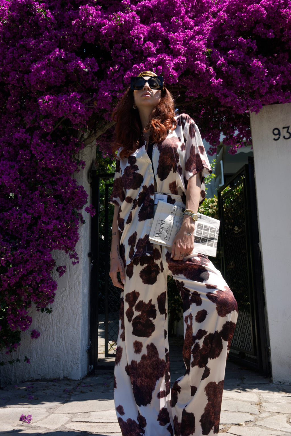 Person wearing a cow print outfit standing in front of purple flowering bushes.