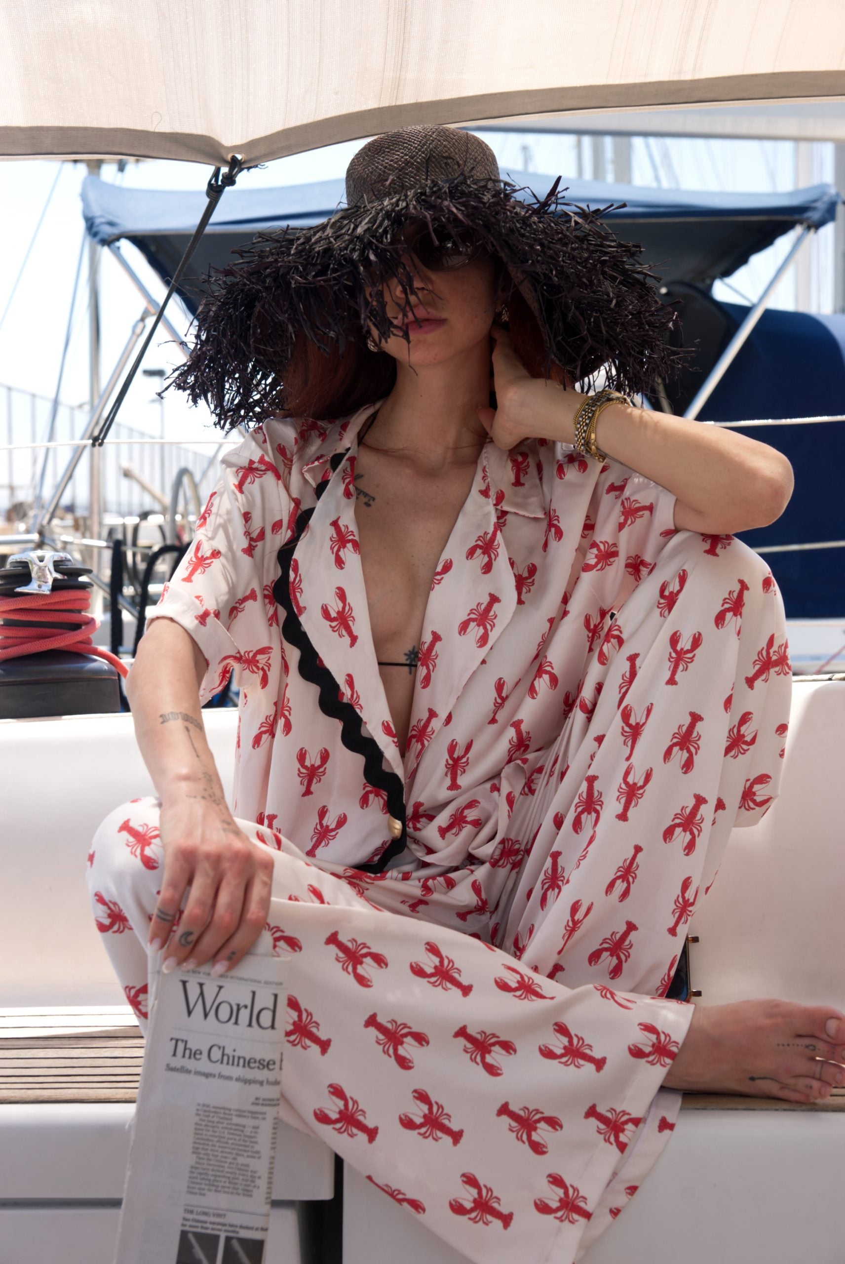 Woman wearing a white outfit with red patterns and a large black hat on a boat.