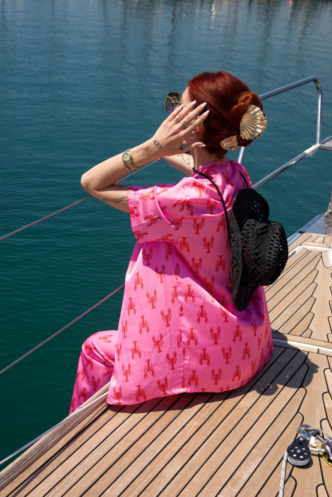 Person in a pink dress with red patterns sitting on a boat deck by the water.
