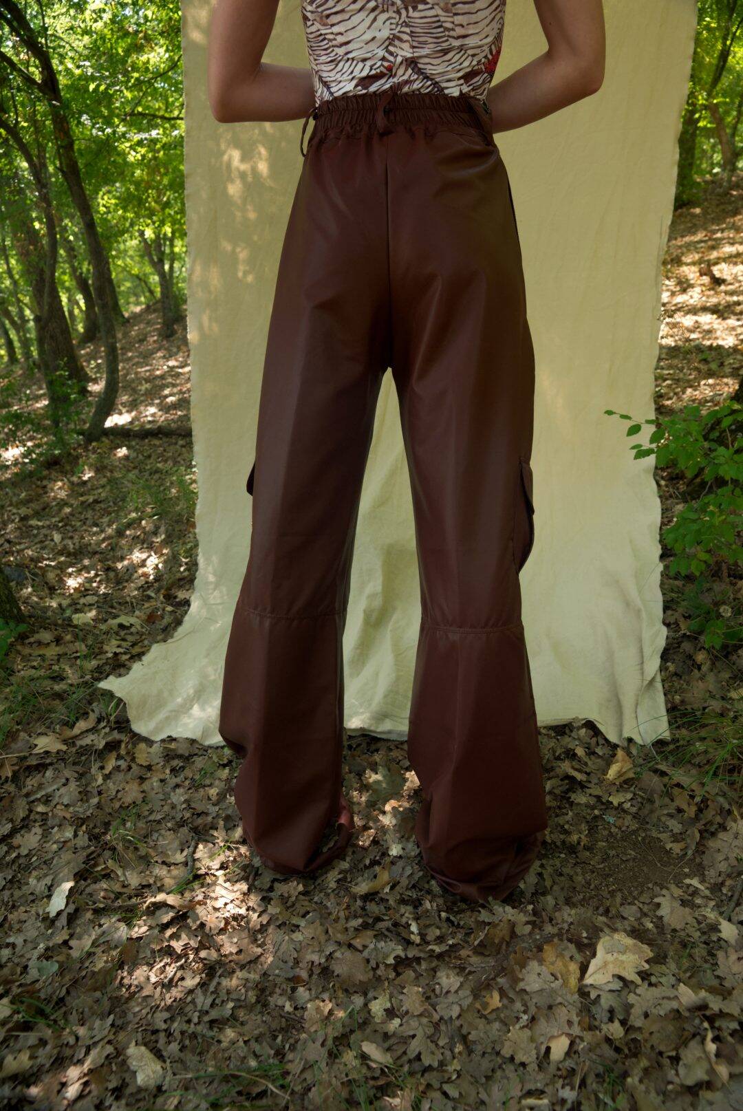 Person wearing brown bell-bottom pants standing in a forest setting with a white curtain.