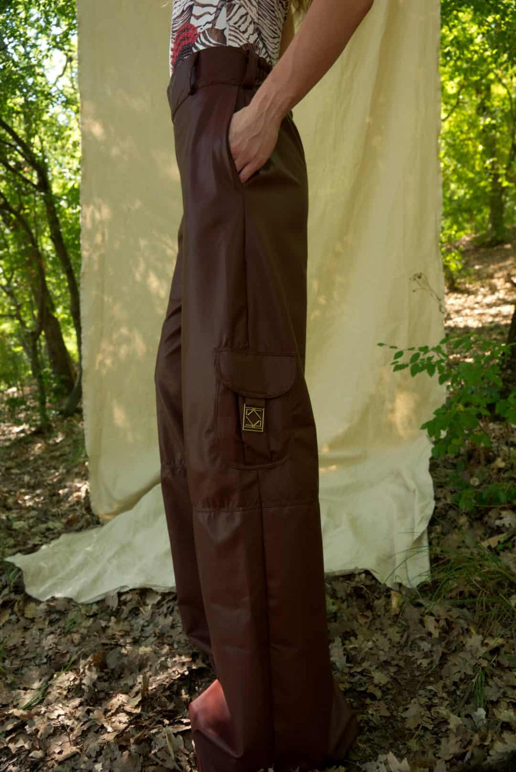 Person wearing brown pants standing in a forest with a white sheet draped over trees.