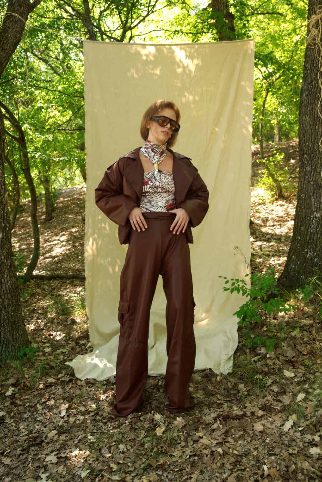 Person wearing a brown outfit standing in front of a white curtain in a forest setting