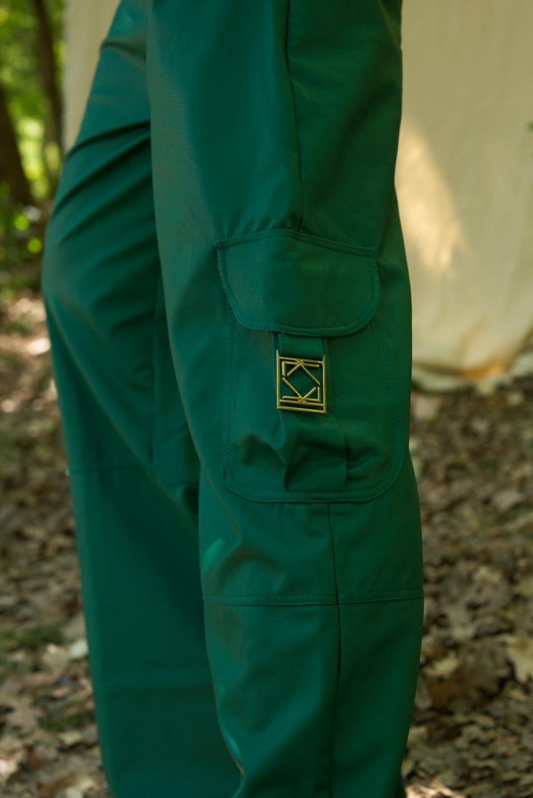 Green pants with a logo patch on a blurred natural background