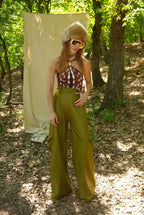 Person in a forest wearing a checkered top and green pants with a large white hat.