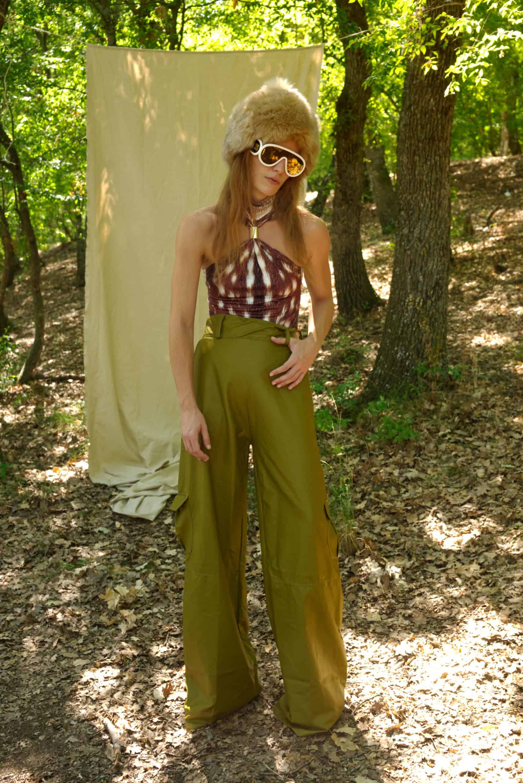 Person in a forest wearing a vintage outfit with wide-leg pants and a headpiece.