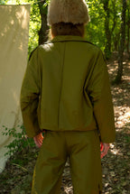 Person wearing a green military-style jacket and pants in a forest setting