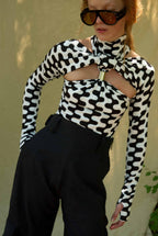 Person wearing a black and white patterned top with cut-out design and sunglasses.