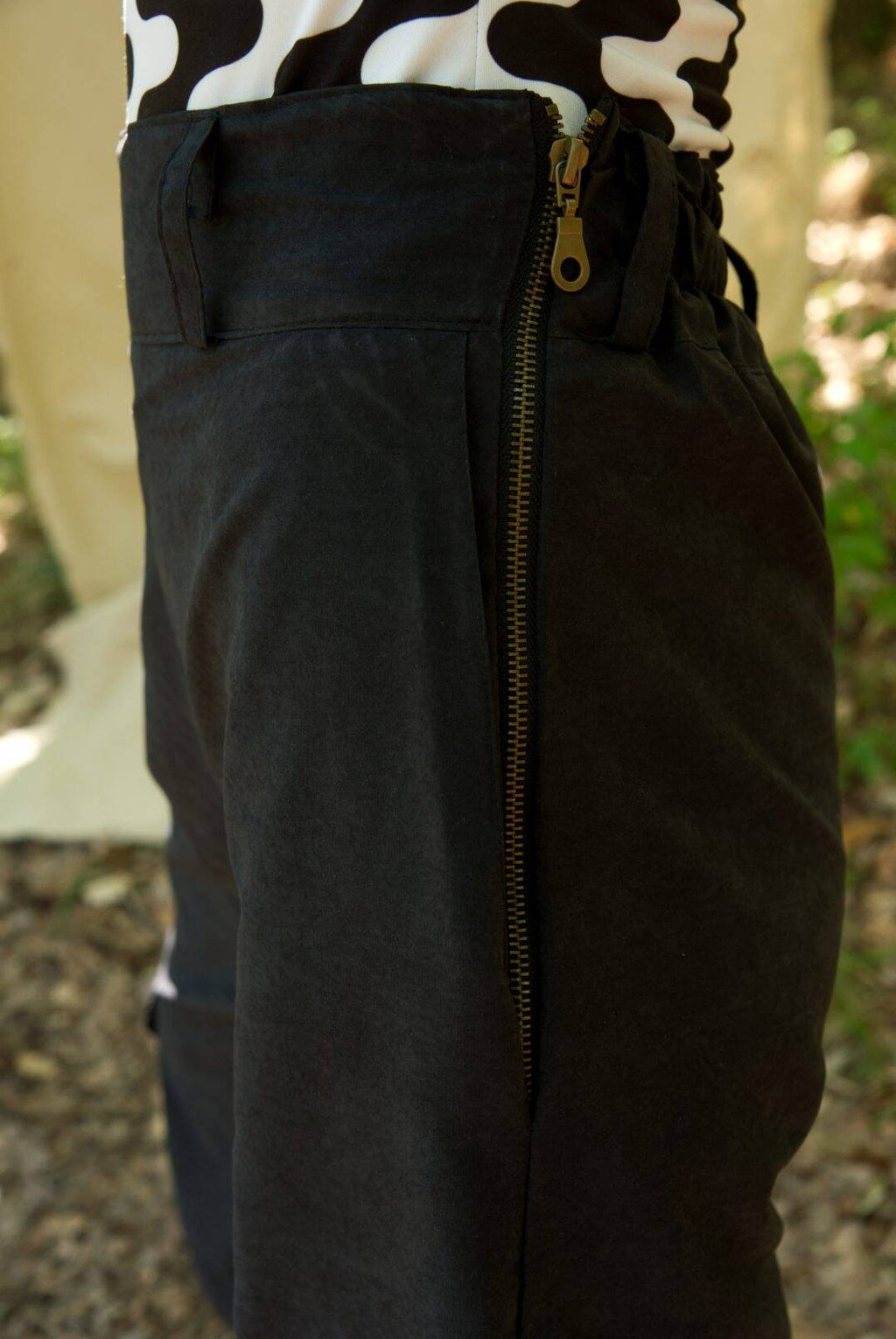 Close-up of dark pants with a zipper, worn over a cow print top.
