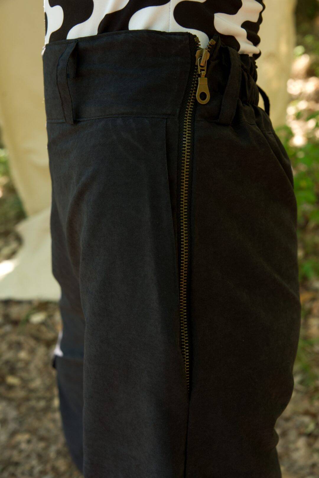 Close-up of dark pants with a zipper, worn over a cow print top.