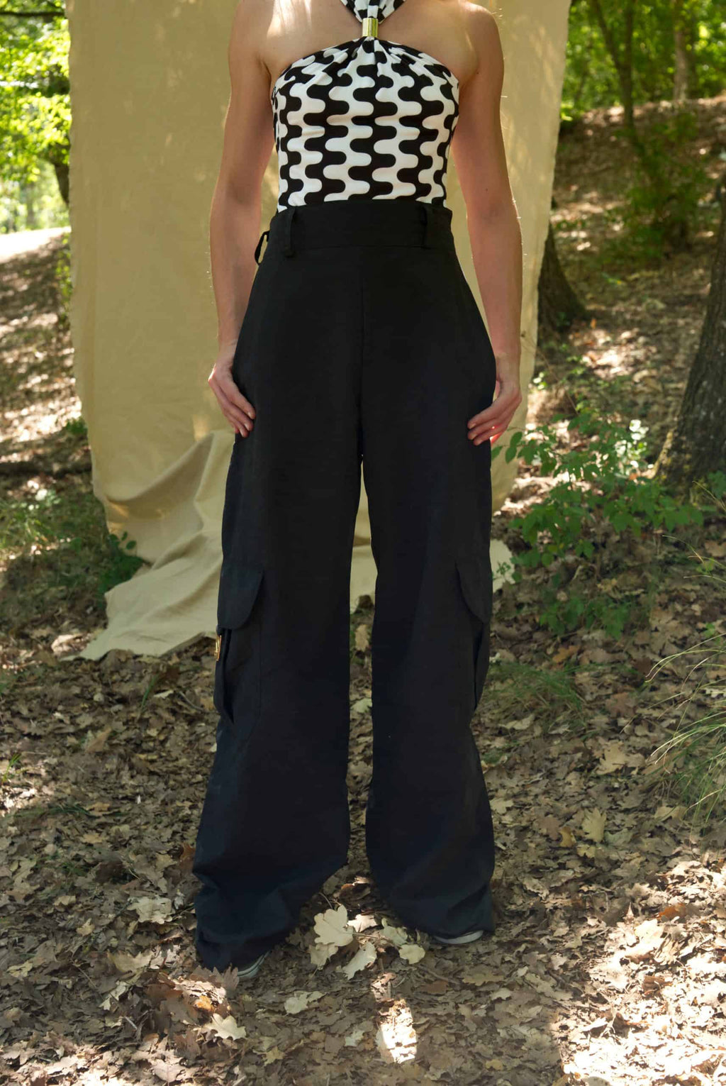 Person wearing a black and white geometric top with black wide-leg pants in a forest setting
