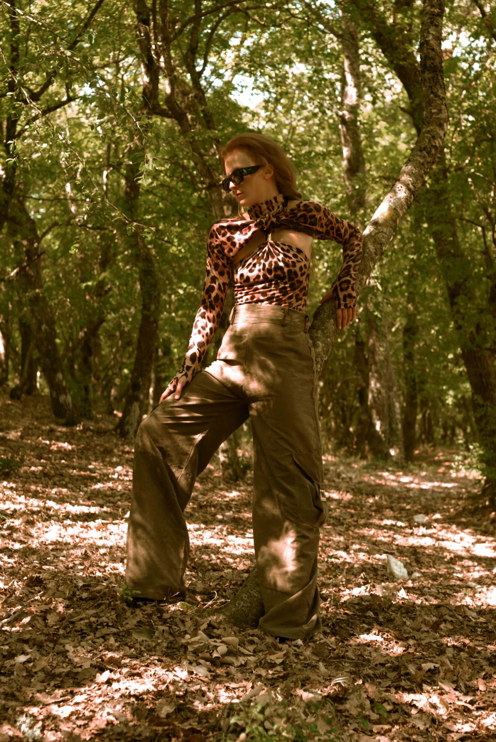 Person wearing a leopard print top and brown pants standing in a forest.