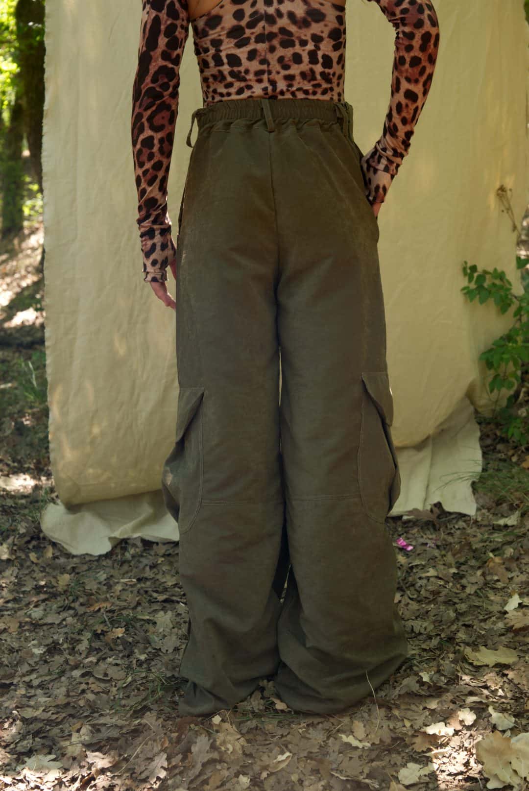 Person wearing a leopard print top and olive green wide-leg pants standing in a natural setting.