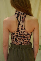 Person wearing a leopard print halter top and green pants against a neutral background