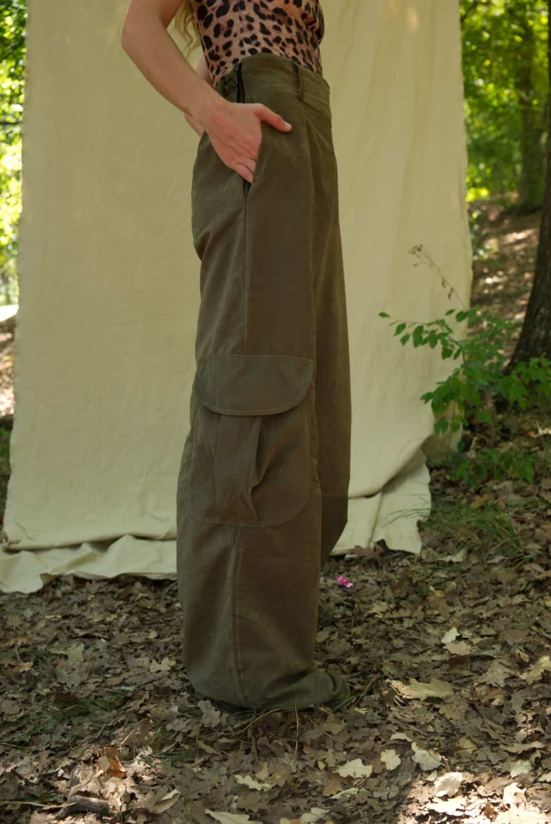 Person wearing olive green cargo pants standing in a forest setting with a white tent in the background.