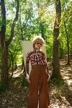 Person in a plaid shirt and brown pants standing in a forest