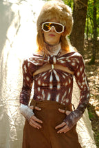 Person wearing a patterned top and brown pants with a fur hat and goggles outdoors.