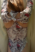 Person wearing a patterned long-sleeve top with a knot detail on a beige background