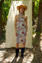 Woman in a patterned dress and straw hat standing in a forest with a white curtain in the background