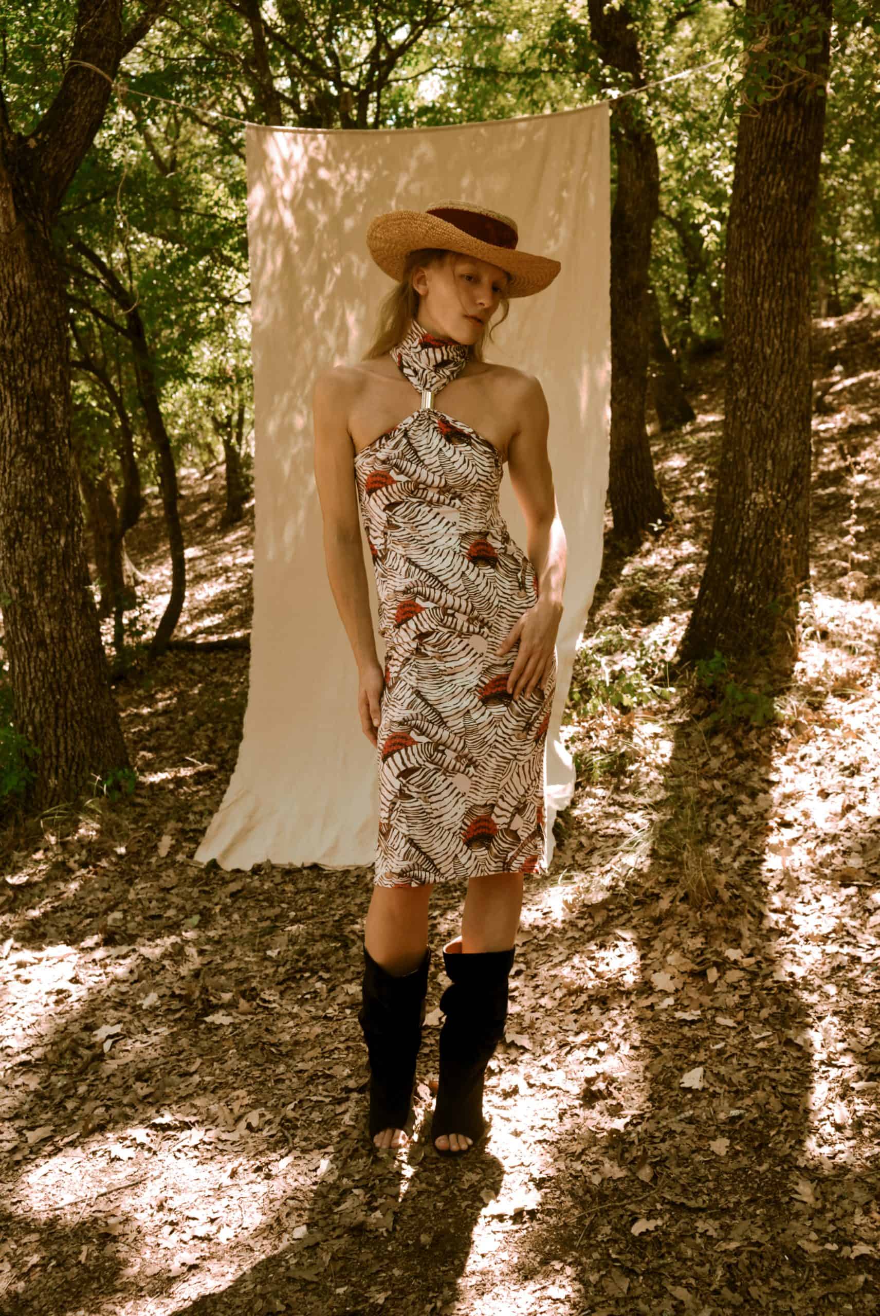 Woman in a patterned dress and cowboy hat standing in a forest