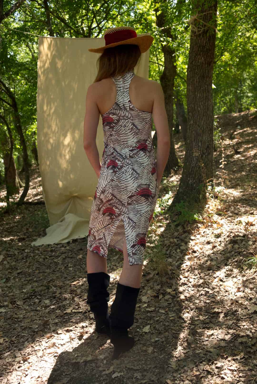 Woman in a patterned dress and hat standing in a forest